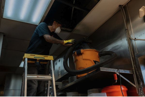 Technician detail-cleaning a kitchen hood line during service